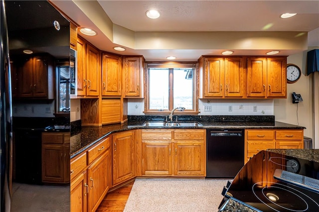 kitchen with sink, backsplash, dark stone counters, black appliances, and light wood-type flooring