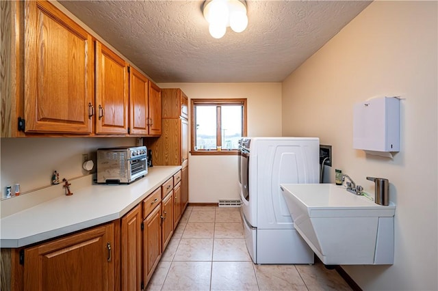 laundry area with cabinets, a textured ceiling, washer and clothes dryer, sink, and light tile patterned flooring