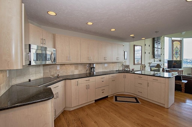 kitchen featuring light brown cabinets, hanging light fixtures, kitchen peninsula, light hardwood / wood-style floors, and black electric cooktop