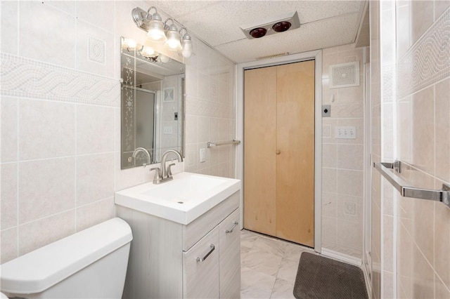 bathroom with vanity, a paneled ceiling, toilet, and tile walls