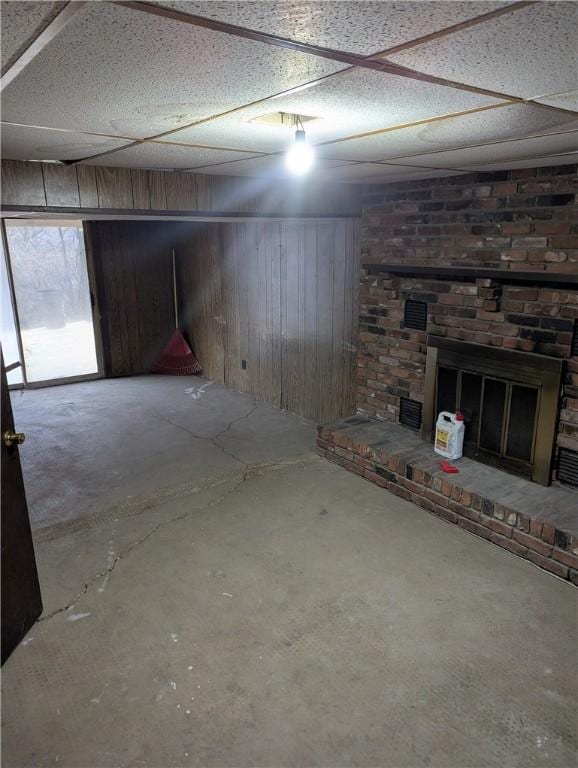 basement featuring a paneled ceiling, wood walls, and a brick fireplace