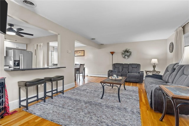 living room featuring light wood-type flooring, baseboard heating, and ceiling fan