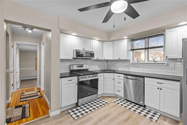 kitchen featuring ceiling fan, stainless steel appliances, a baseboard heating unit, white cabinets, and light wood-type flooring