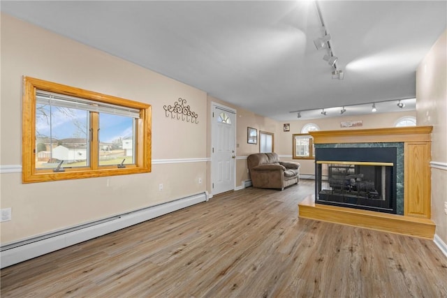 unfurnished living room featuring a multi sided fireplace, track lighting, light hardwood / wood-style flooring, and baseboard heating