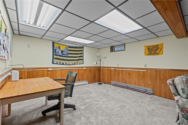 office space with a drop ceiling, carpet floors, baseboard heating, and wood walls