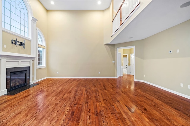 unfurnished living room featuring wood-type flooring and a towering ceiling