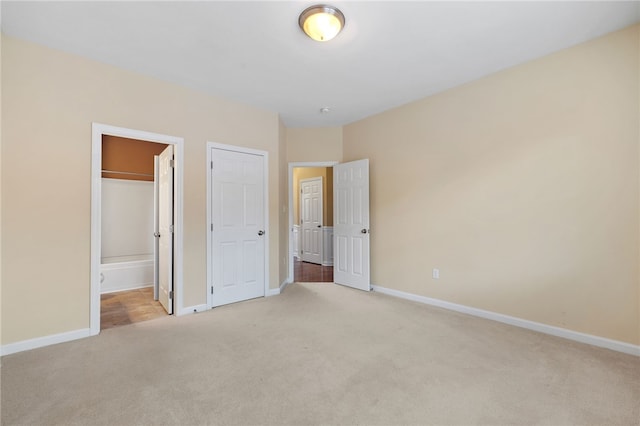 unfurnished bedroom featuring ensuite bath, light carpet, and a closet