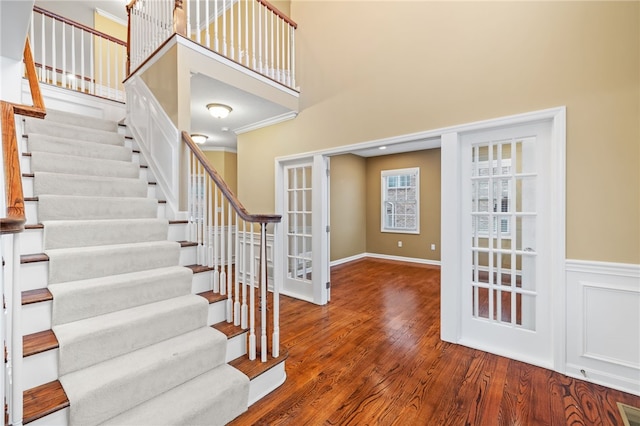 entrance foyer featuring wood-type flooring, a towering ceiling, french doors, and crown molding