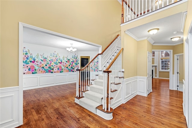 stairs featuring wood-type flooring, ornamental molding, and a chandelier