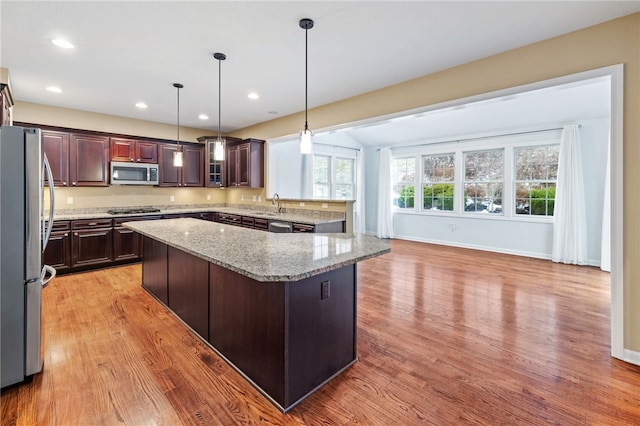 kitchen featuring a center island, hanging light fixtures, light hardwood / wood-style flooring, light stone countertops, and appliances with stainless steel finishes