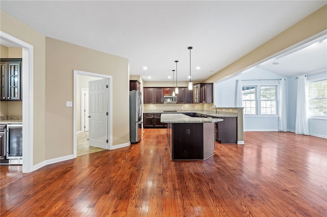 kitchen featuring pendant lighting, a center island, light stone countertops, dark brown cabinetry, and stainless steel appliances