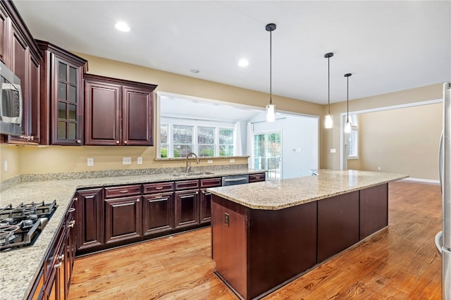 kitchen with a center island, sink, light stone countertops, light wood-type flooring, and stainless steel appliances