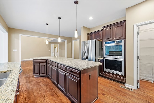 kitchen with a kitchen island, light stone countertops, stainless steel appliances, and hanging light fixtures