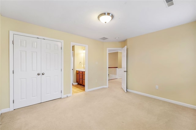 unfurnished bedroom with ensuite bath, a closet, and light colored carpet