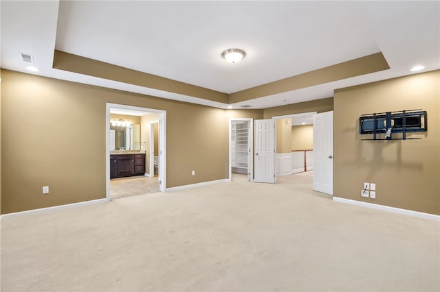 unfurnished bedroom with connected bathroom, light colored carpet, and a raised ceiling