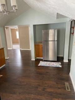 kitchen featuring stainless steel refrigerator, lofted ceiling, dark wood-type flooring, and a textured ceiling