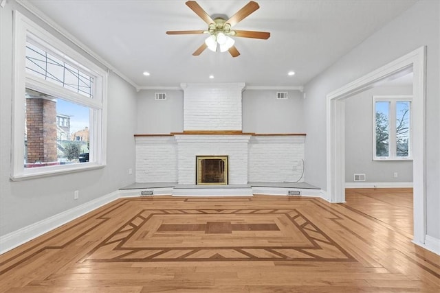 unfurnished living room with light parquet flooring, a brick fireplace, ceiling fan, and crown molding