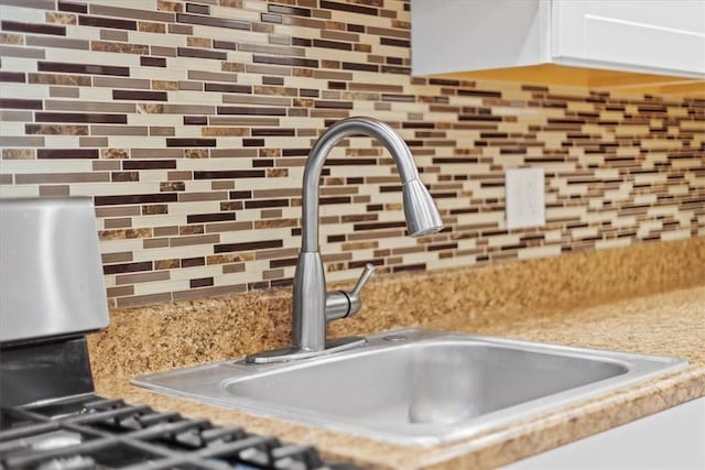 details featuring white cabinets, tasteful backsplash, light stone countertops, and sink