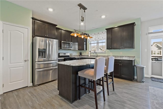 kitchen featuring dark brown cabinetry, hanging light fixtures, light hardwood / wood-style flooring, a kitchen island, and appliances with stainless steel finishes