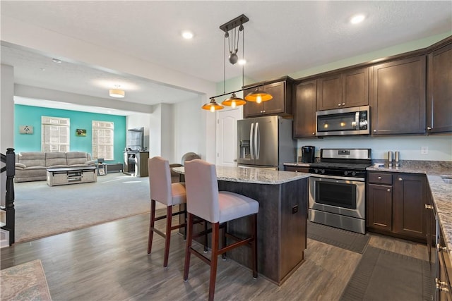 kitchen with appliances with stainless steel finishes, light stone counters, a breakfast bar, a center island, and hanging light fixtures