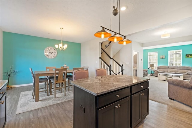 kitchen featuring light stone counters, dark brown cabinets, pendant lighting, light hardwood / wood-style flooring, and a center island