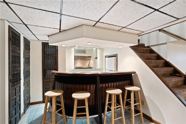 bar with light tile patterned floors and a paneled ceiling