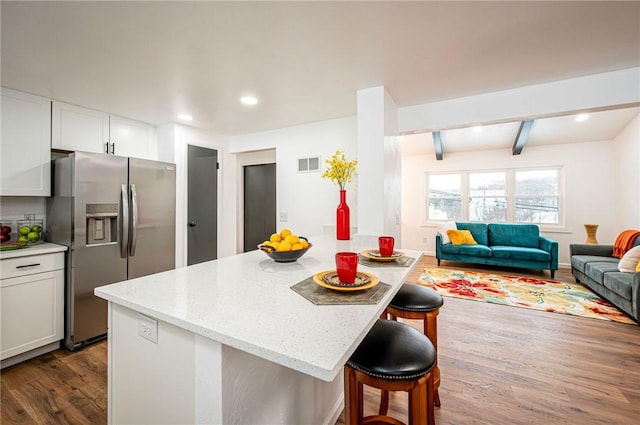 kitchen featuring stainless steel fridge with ice dispenser, beam ceiling, dark hardwood / wood-style flooring, white cabinetry, and a breakfast bar area