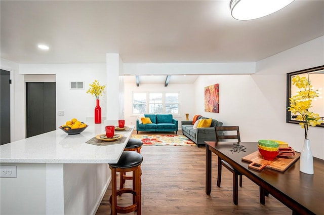 kitchen featuring a kitchen bar, hardwood / wood-style flooring, light stone counters, and beamed ceiling