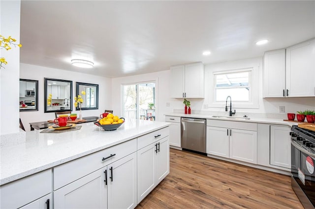 kitchen featuring light wood-type flooring, black gas range oven, sink, dishwasher, and white cabinetry