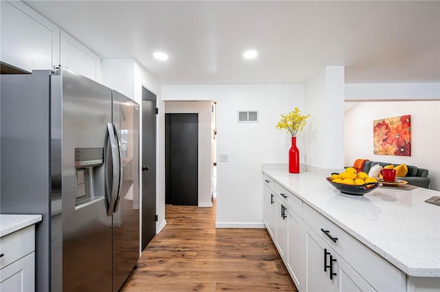 kitchen with white cabinetry, stainless steel fridge, light stone countertops, and hardwood / wood-style flooring