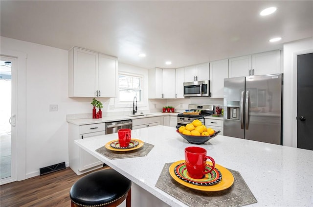 kitchen with appliances with stainless steel finishes, a kitchen breakfast bar, dark wood-type flooring, sink, and white cabinets