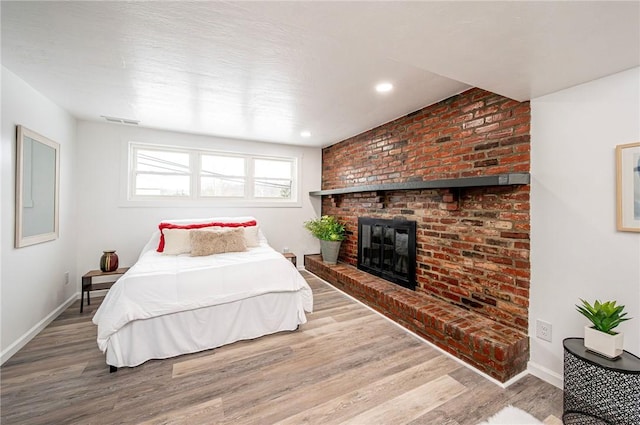 bedroom with hardwood / wood-style flooring and a brick fireplace