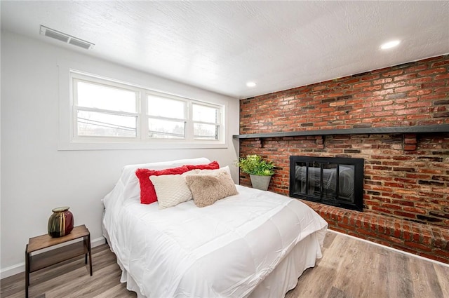 bedroom with hardwood / wood-style floors and a brick fireplace