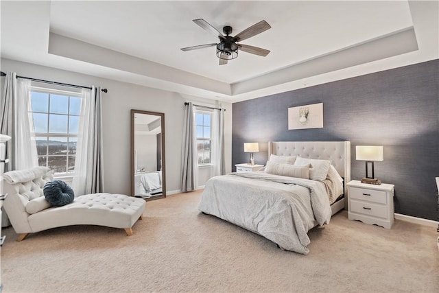 carpeted bedroom with a tray ceiling, multiple windows, and ceiling fan