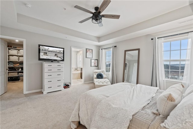 carpeted bedroom featuring ceiling fan, a raised ceiling, connected bathroom, and multiple windows