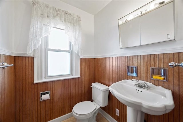 bathroom featuring toilet, wooden walls, and sink