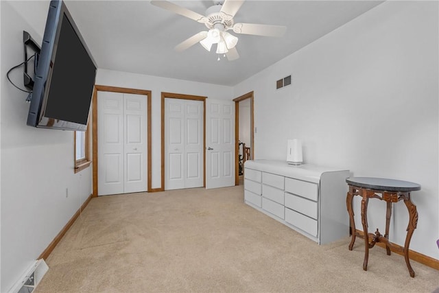 bedroom with ceiling fan, light carpet, and two closets