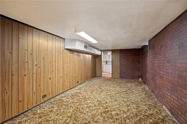 basement with carpet, a textured ceiling, wooden walls, and brick wall