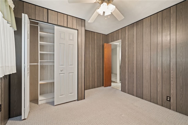 unfurnished bedroom with light carpet, a closet, ceiling fan, and wood walls