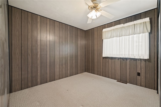 empty room featuring ceiling fan, carpet, and wood walls