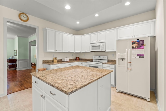 kitchen with light tile patterned flooring, white appliances, white cabinets, a kitchen island, and light stone counters