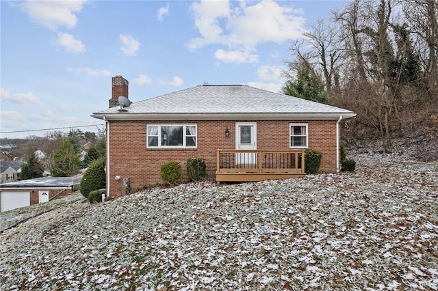 rear view of property with brick siding, a chimney, a wooden deck, and roof with shingles