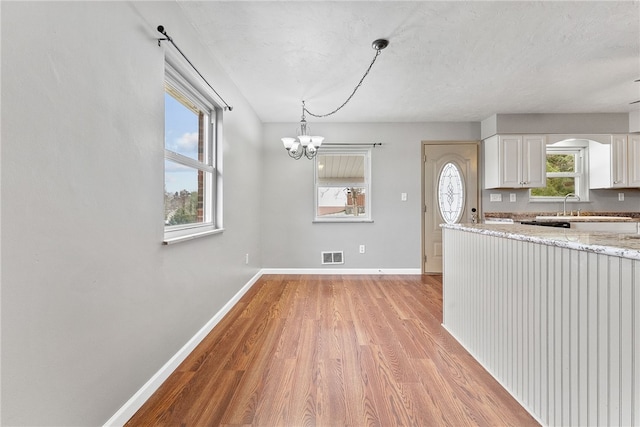 kitchen with light stone countertops, decorative light fixtures, light hardwood / wood-style flooring, a notable chandelier, and white cabinetry