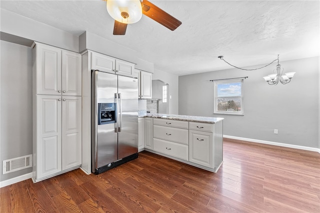 kitchen featuring dark wood-type flooring, ceiling fan with notable chandelier, kitchen peninsula, stainless steel fridge, and white cabinetry