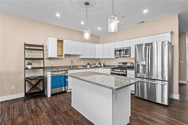 kitchen with appliances with stainless steel finishes, light stone counters, white cabinets, a kitchen island, and hanging light fixtures