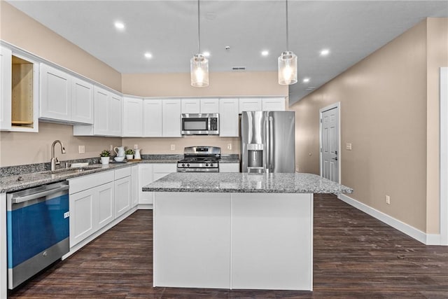 kitchen with light stone countertops, white cabinetry, a center island, stainless steel appliances, and pendant lighting