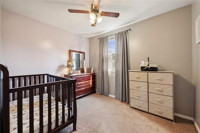 bedroom featuring ceiling fan, light colored carpet, and a nursery area