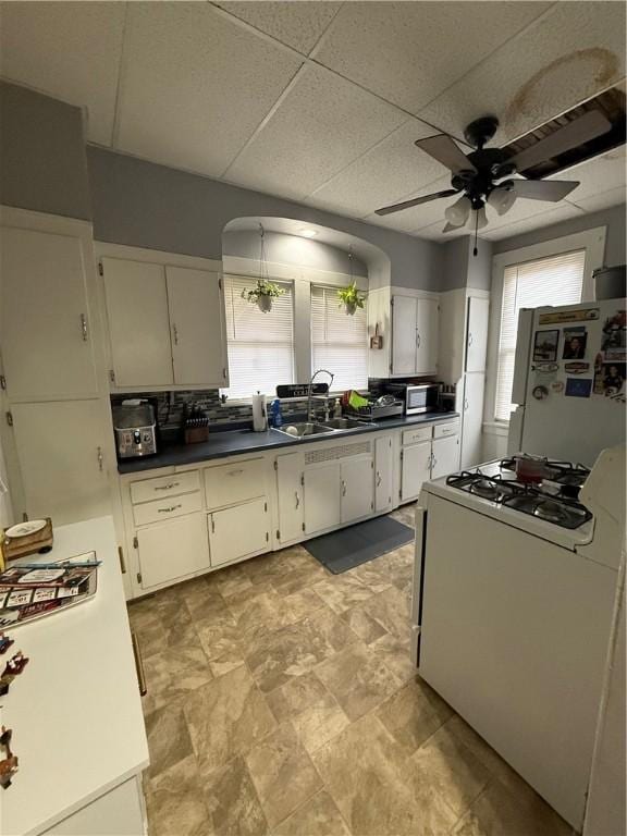 kitchen with a drop ceiling, white appliances, ceiling fan, sink, and white cabinets