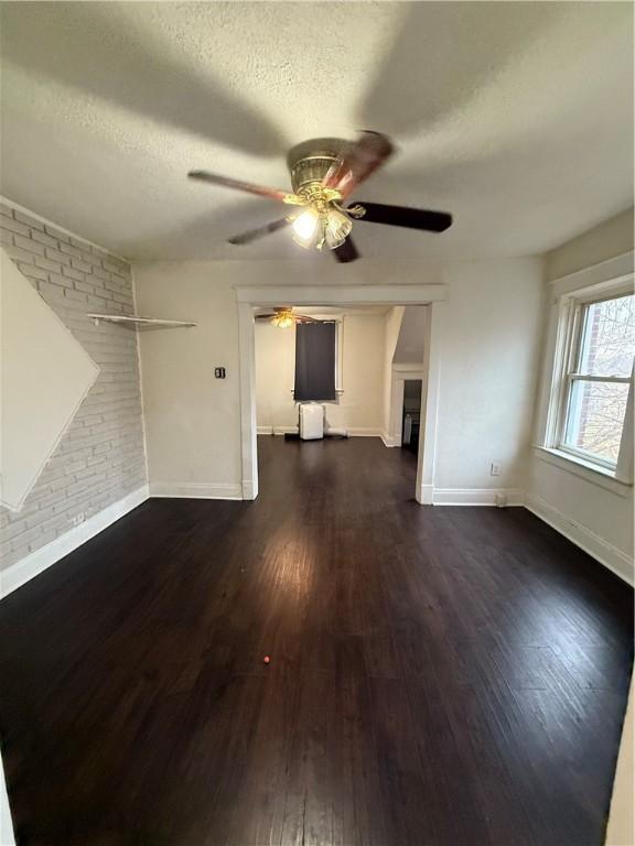 unfurnished living room with ceiling fan, a brick fireplace, dark hardwood / wood-style flooring, brick wall, and a textured ceiling