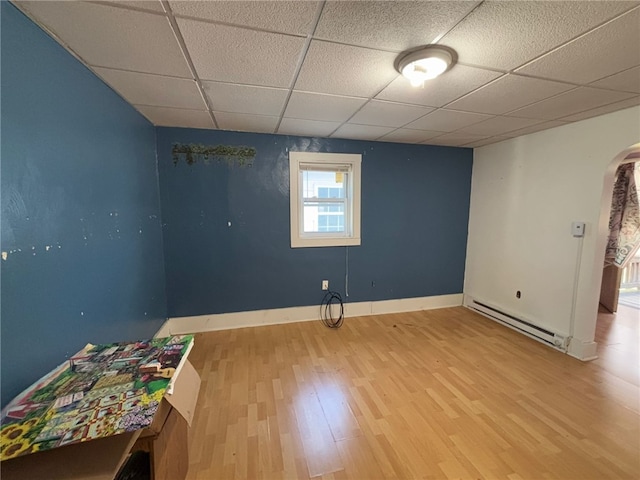 spare room featuring a drop ceiling, a baseboard radiator, and hardwood / wood-style flooring